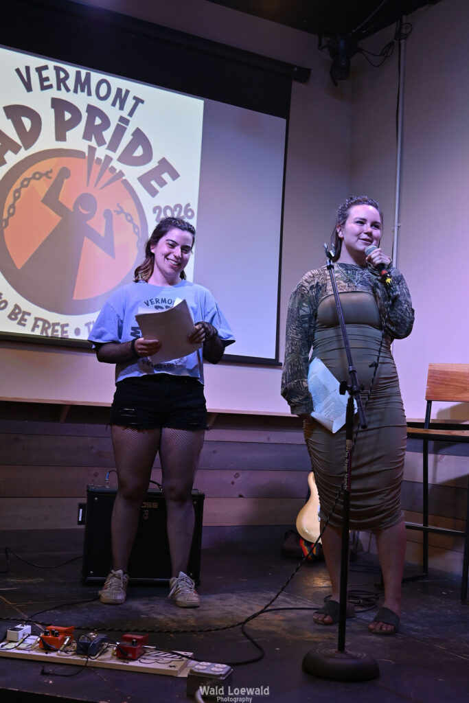 Neilah and Esme, MadFreedom Advocates staff, standing on stage with mic in front of Mad Pride 2026 logo