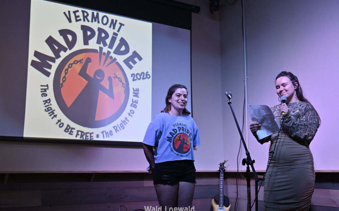 Neilah and Esme, MadFreedom Advocates staff, standing on stage with mic in front of Mad Pride 2026 logo