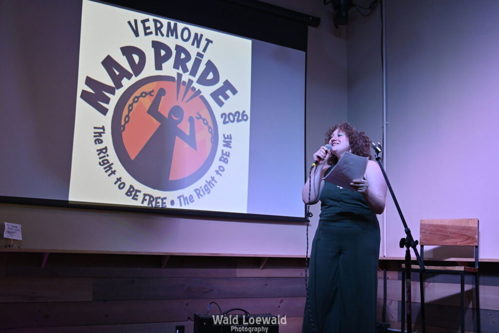 Performer behind a mic in front of the Mad Pride 2026 logo