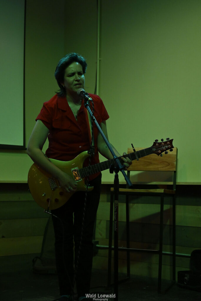 Performer playing guitar behind a mic