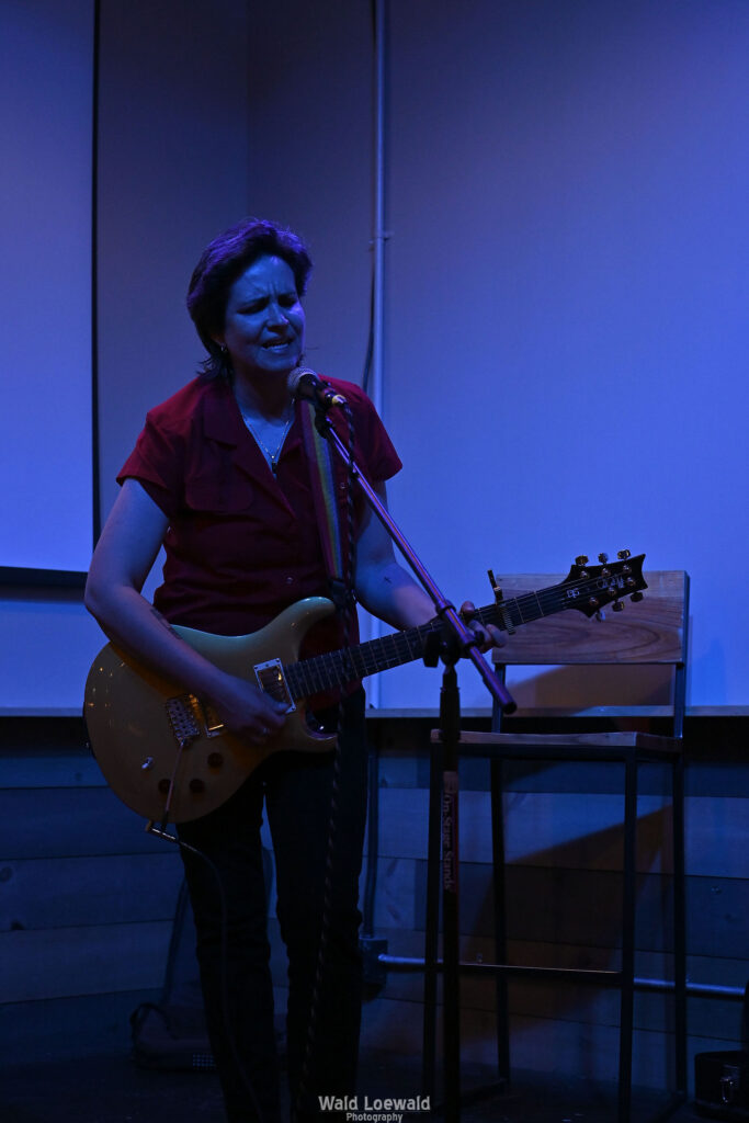 Performer playing guitar behind a mic