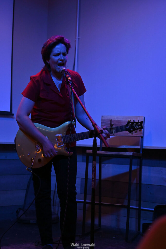 Performer playing guitar behind a mic