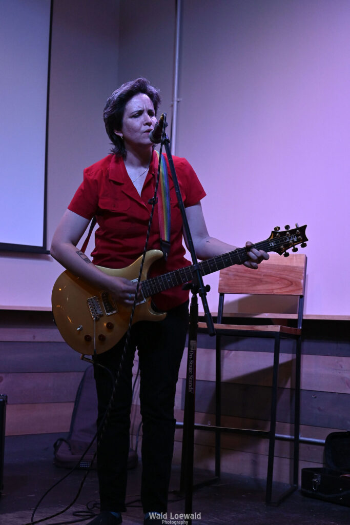 Performer playing guitar behind a mic