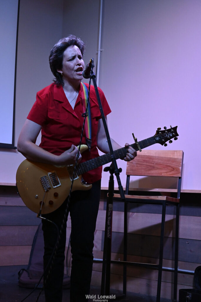 Performer playing guitar behind a mic