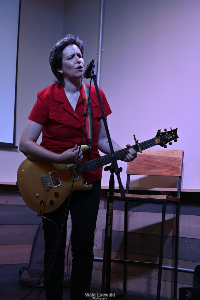 Performer playing guitar behind a mic