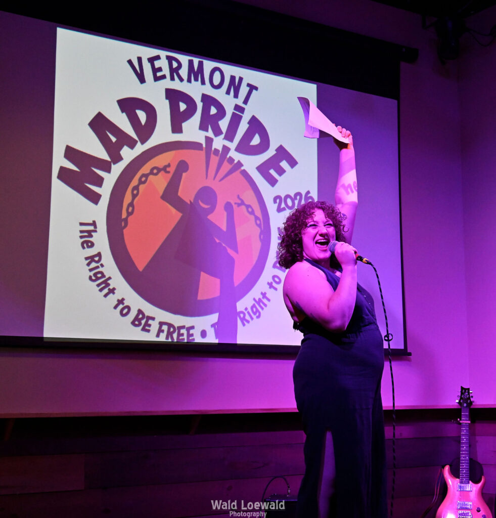 Performer holding a mic in front of the Mad Pride 2026 logo