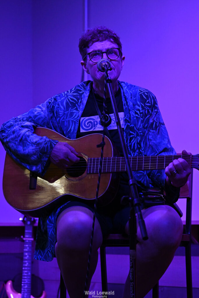 Chris Hansen sitting behind a mic playing guitar