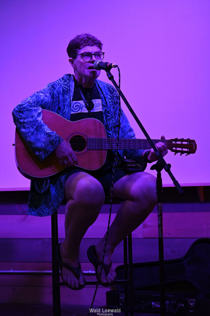 Chris Hansen sitting behind a mic playing guitar
