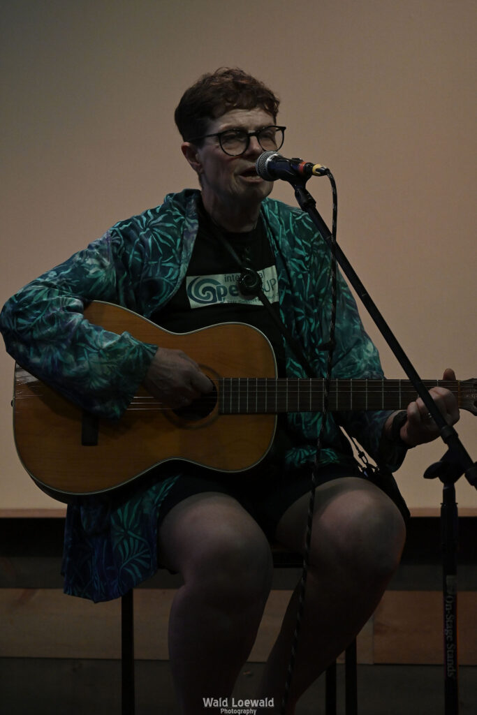 Chris Hansen sitting behind a mic playing guitar