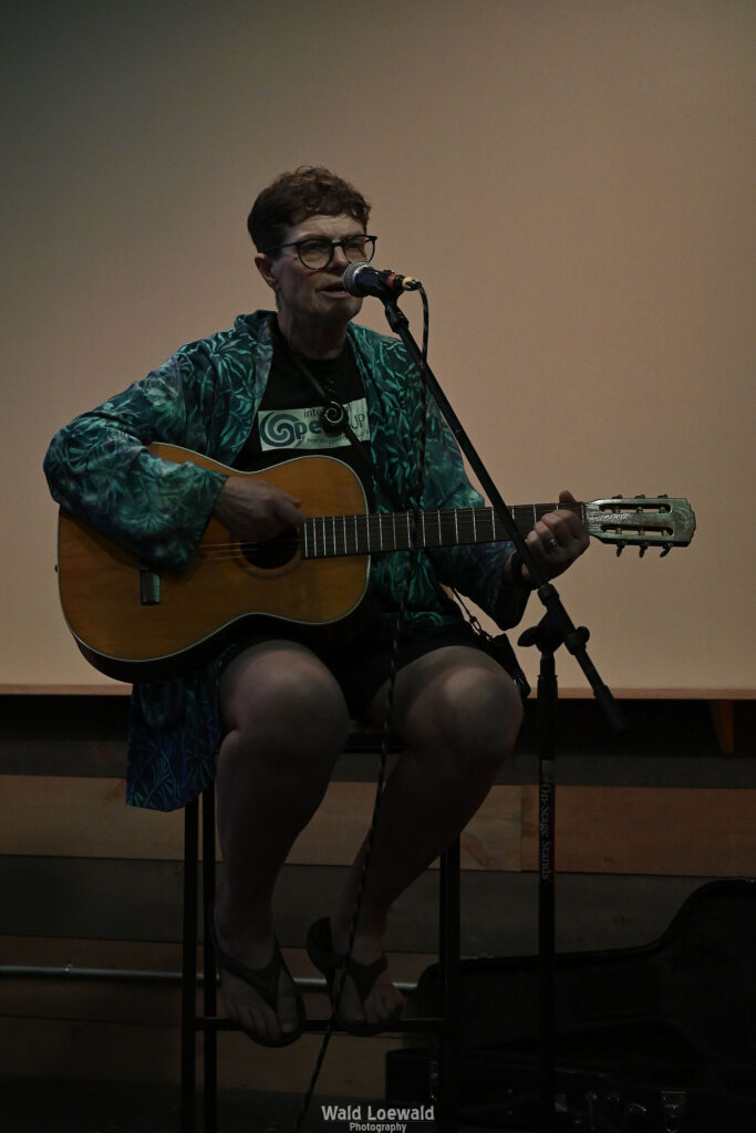 Chris Hansen sitting behind a mic playing guitar