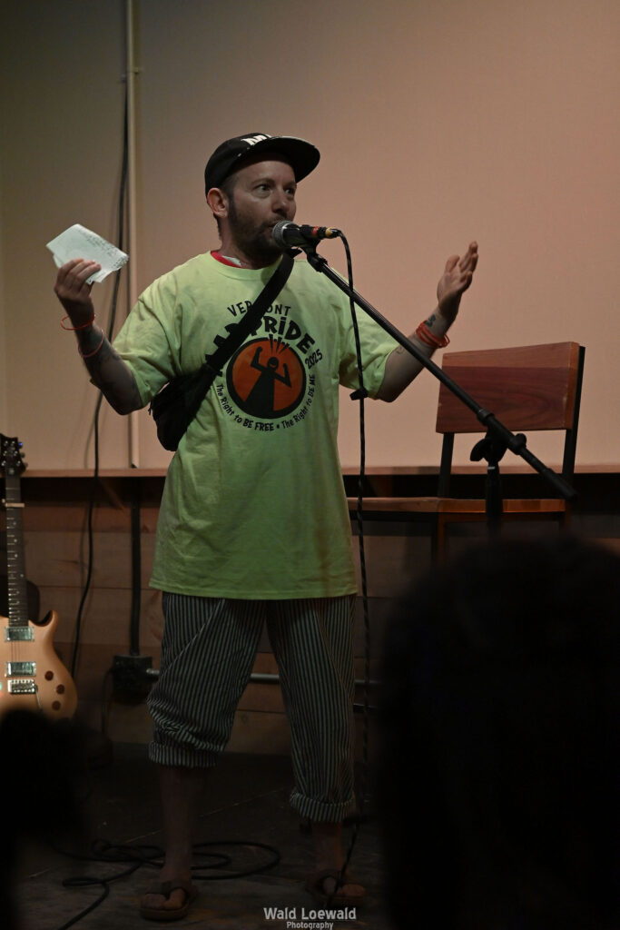 Cal Moen standing behind a mic, in a Mad Pride 2025 shirt