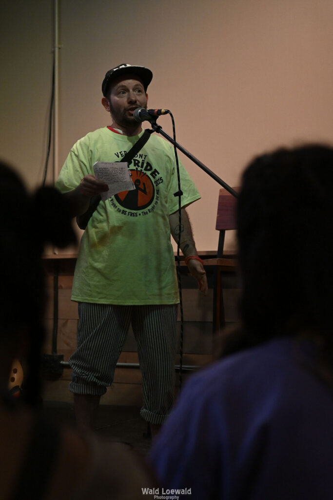 Cal Moen standing behind a mic, in a Mad Pride 2025 shirt