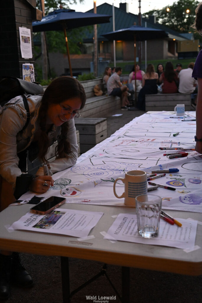 People signing white banner with colored markers