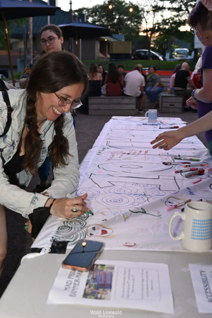 People signing white banner with colored markers