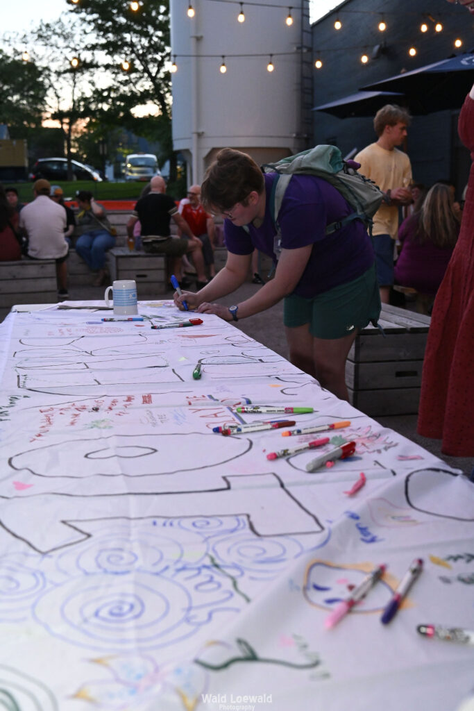People signing white banner with colored markers