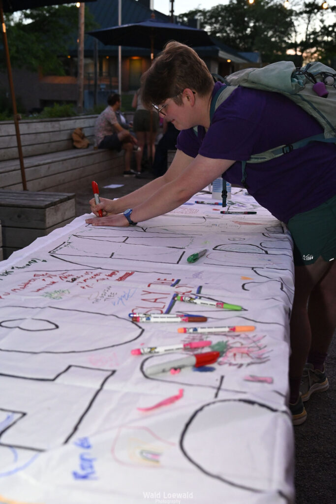 People signing white banner with colored markers