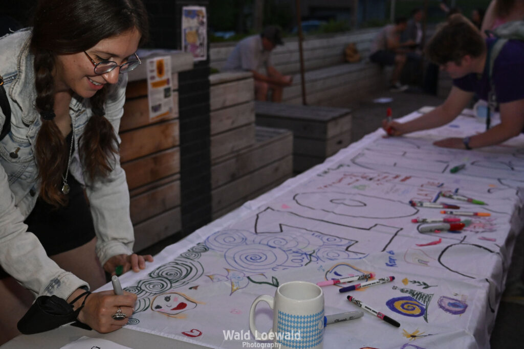 People signing white banner with colored markers