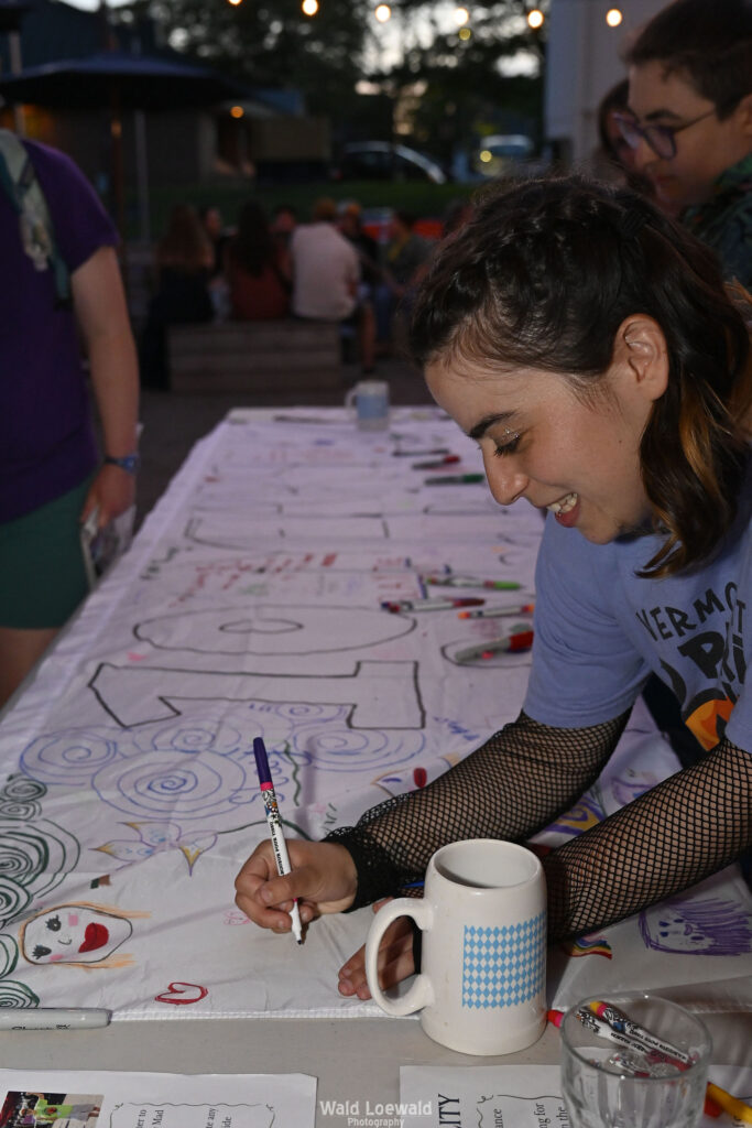 People signing white banner with colored markers