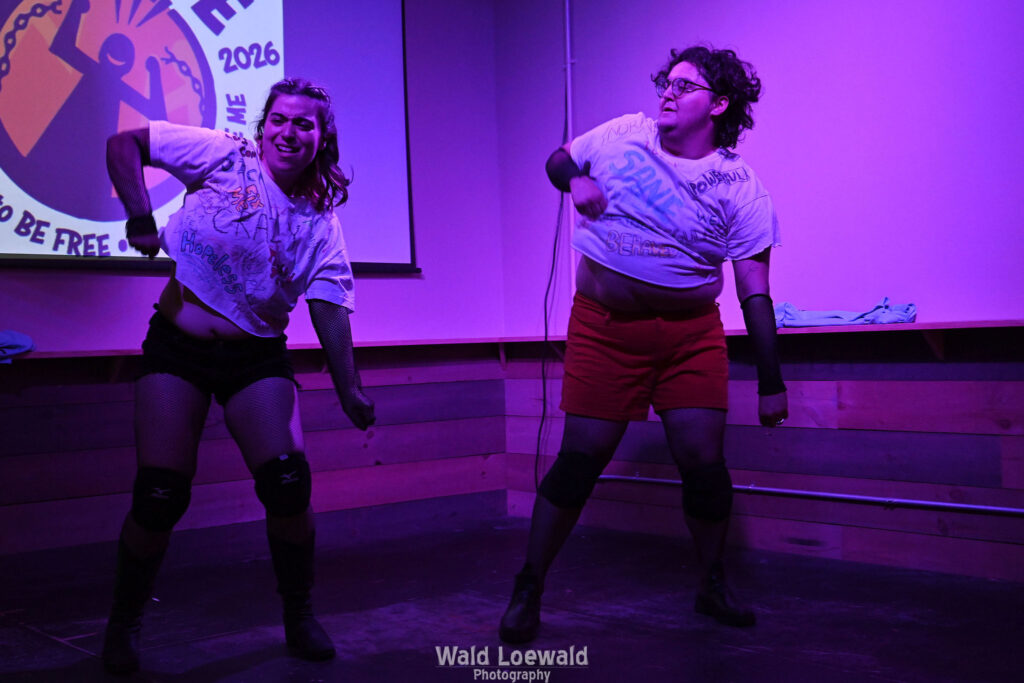 Neilah and friend in matching Mad Pride shirts performing in pink lighting