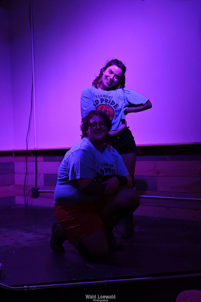 Neilah and friend in matching Mad Pride shirts performing in pink lighting