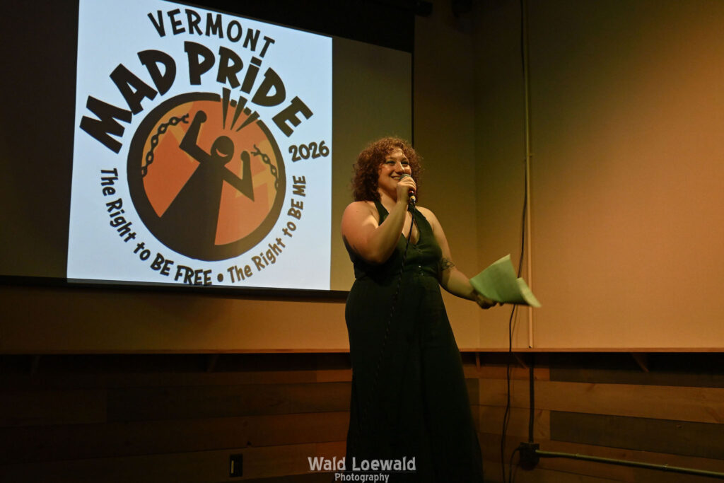 Performer standing with mic in hand, in front of Mad Pride 2026 logo
